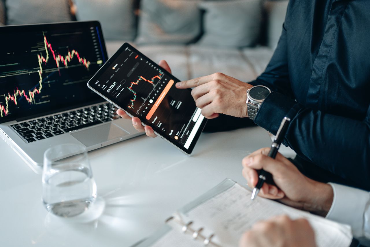 Two professionals analyzing stock graphs on digital devices in a modern business setting.